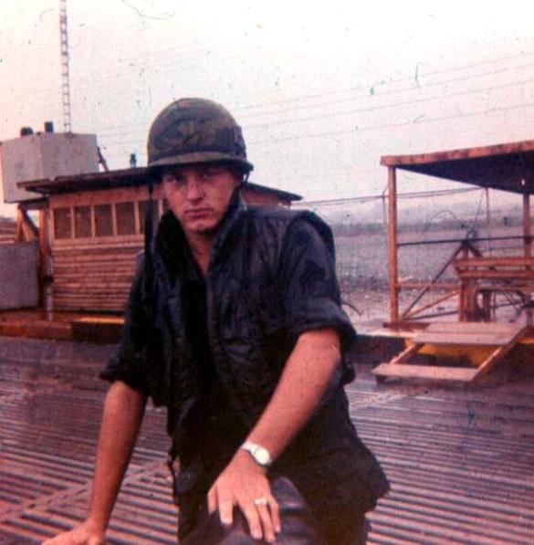 Sgt. Krabbenhoeft Standing On The APC Parking Area With Weapons Cleaning  Shelter On Right And Shower On Left 