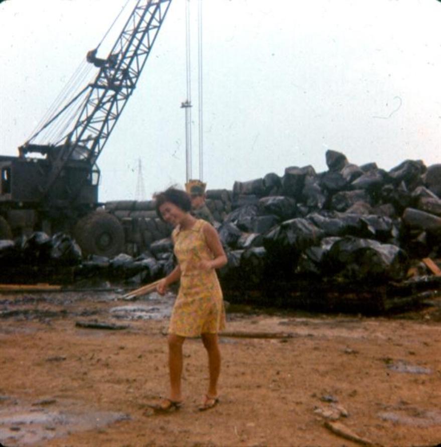  This photo is also on one of Al Krabbenhoeft's pages.  Thought it was worth a second look.  This civilian Newport worker is looking at the site where James Lake was killed on the May 12, 1968 rocket attack.  She is smiling because her picture was being taken.  Look in the background. Those are broken and damaged barrels. - A close look shows evidence of orange and white stripes